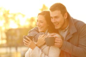 happy couple looking away holding coffee mugs